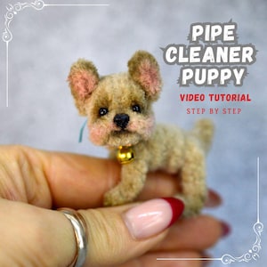 May include: A small brown and white pipe cleaner puppy with pink ears and a gold bell collar. The puppy is being held in a hand. The text "PIPE CLEANER PUPPY VIDEO TUTORIAL STEP BY STEP" is in the upper right corner of the image.