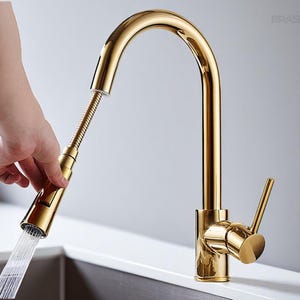 Könnte beinhalten: Ein goldfarbener Küchenarmatur mit ausziehbarem Sprühkopf. Der Wasserhahn hat einen gebogenen Auslauf und einen Einhebelgriff. Wasser fließt aus dem Sprühkopf. Der Wasserhahn ist aus Metall und hat eine glänzende Oberfläche. Der Wasserhahn ist auf einer Arbeitsplatte montiert.