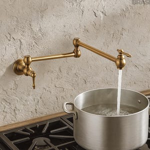 Puede incluir: Un grifo de llenado de ollas de latón con un brazo articulado está montado en una pared texturizada. El agua fluye del grifo a una olla de acero inoxidable sobre una estufa de gas. El grifo tiene un diseño vintage.