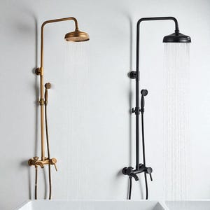 Puede incluir: Dos juegos de ducha, uno en latón antiguo y otro en negro mate, están montados en una pared blanca. Cada uno tiene un cabezal de ducha redondo, una ducha de mano y un grifo. El accesorio de latón tiene un tono dorado cálido, mientras que el negro ofrece un contraste elegante y moderno.