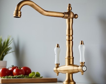 Puede incluir: Un grifo de cocina de latón con un caño curvo y manijas de porcelana blanca. El grifo tiene un diseño clásico con una estética vintage. La marca "BRASIFY" es visible en la esquina superior derecha.