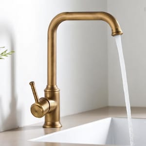 May include: A bronze-colored kitchen faucet with a curved spout and a single lever handle. Water flows from the faucet into a white sink. The faucet is set against a neutral-toned countertop and a white wall.