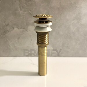 May include: A gold-toned drain stopper with a decorative top and a white ceramic ring. The drain stopper is made of metal and has a cylindrical shape.