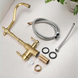 May include: A new, uninstalled brass kitchen faucet with a curved spout, two handles, and various components. Includes flexible hoses, rubber washers, and a mounting nut. The faucet has a vintage style.
