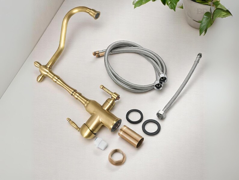 May include: A new, uninstalled brass kitchen faucet with a curved spout, two handles, and various components. Includes flexible hoses, rubber washers, and a mounting nut. The faucet has a vintage style.