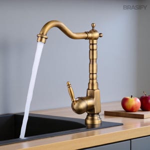 Puede incluir: Un grifo de cocina de latón antiguo con un caño curvo y una manija de palanca. El agua fluye del caño a un fregadero negro. El grifo tiene una columna decorativa y un diseño clásico. La palabra "BRASIFY" es visible en la esquina superior derecha.
