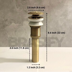 May include: A gold-toned bathroom sink drain with a decorative top. The drain is 8.6 inches (22 cm) tall, 4.6 inches (11.8 cm) wide, and 1.2 inches (3.2 cm) in diameter.
