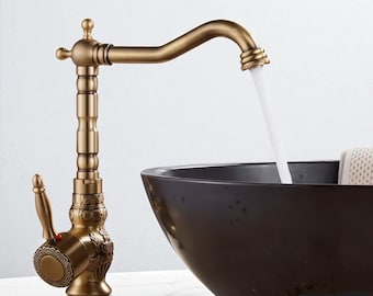 May include: An antique-style brass faucet with intricate floral and geometric patterns. The faucet is positioned over a dark brown, oval-shaped sink. Water flows from the faucet's spout. The brand name "BRASIFY" is visible in the upper right corner.