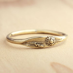 May include: A gold ring with a delicate floral design. The ring features a small flower with a leaf on either side.