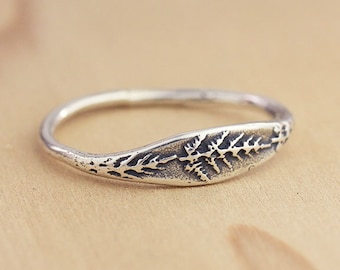 Puede incluir: Un anillo de plata con un diseño de helecho. El anillo es simple y delicado, lo que lo convierte en una gran pieza de joyería para el día a día.