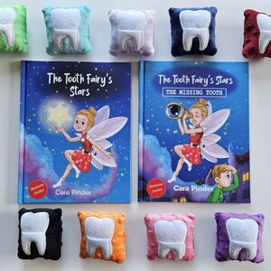 Op de afbeelding: Een assortiment kleurrijke tandvormige kussens en twee kinderboeken getiteld "The Tooth Fairy's Stars". De boeken bevatten illustraties van een fee en een nachthemel. De kussens zijn in verschillende kleuren, waaronder groen, blauw, paars en rood.