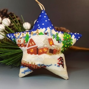 May include: A blue, white, and brown beaded star ornament with a winter scene. The ornament features a small house, a tree, and snow.
