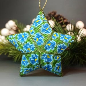 May include: A beaded star ornament with a green and blue floral pattern. The star is 3-dimensional and has a gold loop for hanging.
