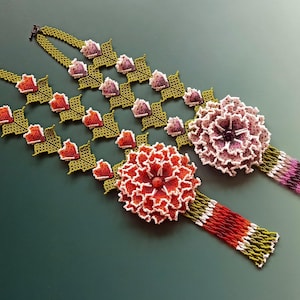 May include: Two beaded necklaces with floral designs. The necklaces are made with green, white, pink, and red beads. The necklaces feature large flower accents.