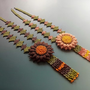 Puede incluir: Dos collares de cuentas con detalles de flores. Un collar es verde, marrón y naranja, y el otro es rosa, verde y amarillo.