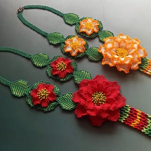 May include: Two beaded necklaces with green leaves and colorful flower accents. One necklace has red flowers and the other has orange flowers.