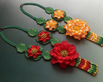 May include: Two beaded necklaces with green leaves and colorful flower accents. One necklace has red flowers and the other has orange flowers.