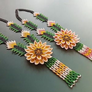 May include: Two beaded necklaces with green, black, white, and yellow beads. Each necklace features a large beaded flower with a yellow center and pink and white petals.