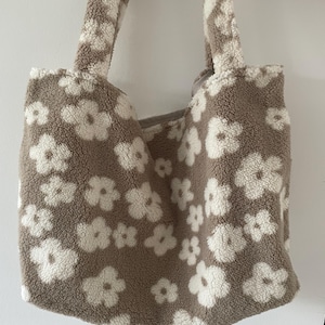May include: A brown and white fluffy tote bag with a floral pattern. The bag has two handles.