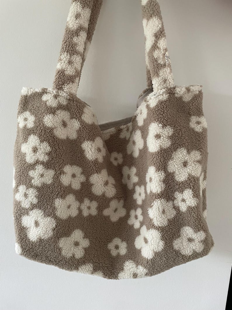 May include: A brown and white fluffy tote bag with a floral pattern. The bag has two handles.