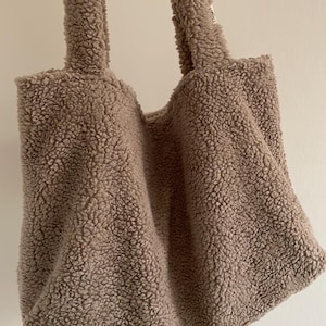 May include: A light brown fluffy tote bag with a small white tag that says "E.D.M.W.H."