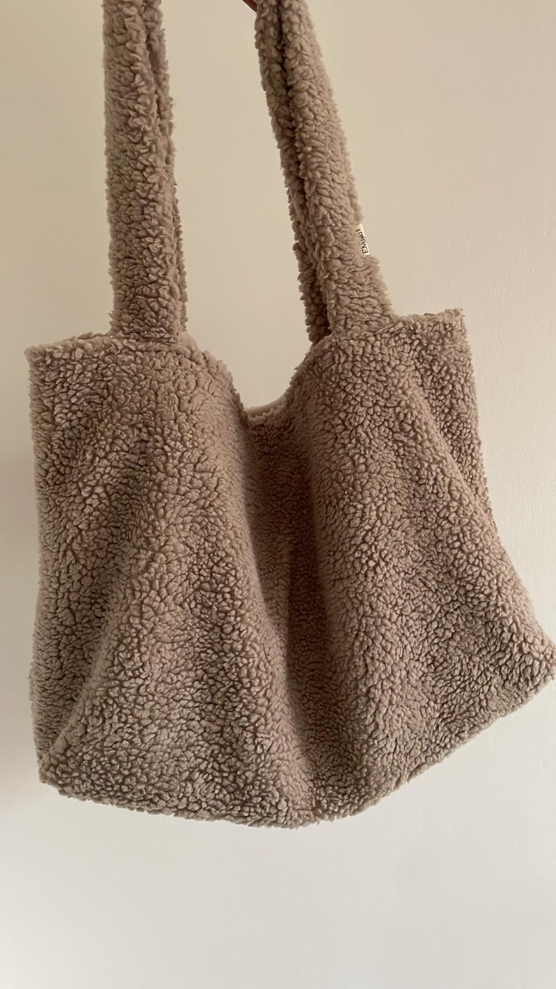 May include: A light brown fluffy tote bag with a small white tag that says "E.D.M.W.H."