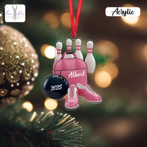 May include: A pink acrylic bowling ornament with a red ribbon for hanging. The ornament features a bowling ball with "2025", a bowling bag with "Albert", bowling pins, and bowling shoes. The word "Acrylic" is also visible.