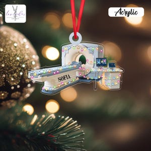 Könnte beinhalten: Weihnachtsschmuck aus Acryl in Form eines CT-Scanners, verziert mit bunten Lichtern. Der Name "SOFIA" ist auf dem Scannerbett aufgedruckt. Der Schmuck hängt an einem roten Band. Das Wort "Acrylic" ist oben rechts aufgedruckt.