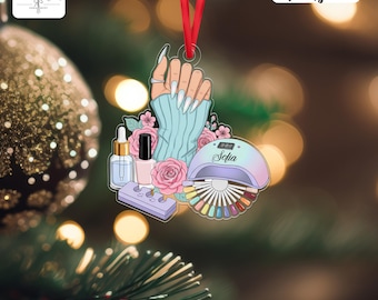 May include: An acrylic hanging ornament featuring a hand with long white nails wearing a light blue sweater, surrounded by pink roses, a nail polish bottle, a cuticle oil dropper, a purple nail file, and a nail lamp with the name Sofia.