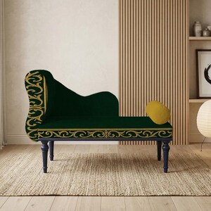 May include: A dark green chaise lounge with gold decorative trim and a matching yellow cushion. The chaise lounge has dark blue legs and is placed on a woven rug. The background includes a wooden slatted wall and a framed artwork.