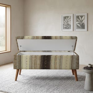 Peut inclure: Un banc de rangement rectangulaire avec un couvercle à charnière en position ouverte, doté d'un revêtement en tissu texturé à rayures verticales dans des tons marron, beige et crème, soutenu par quatre pieds en bois fuselés finition marron.