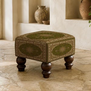 May include: A square ottoman featuring a deep olive green fabric with an intricate, symmetrical floral pattern in shades of cream and gold. The piece is supported by four dark brown, rounded wooden bun feet that provide a sturdy base.