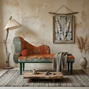 May include: An orange chaise lounge with floral patterns and green legs sits on a gray rug. A wooden coffee table holds a cup and stones. A tall lamp with a paper shade and a framed textile art piece complete the cozy, bohemian-style living room.