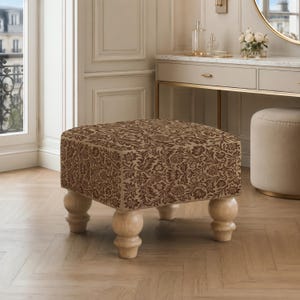 May include: A square ottoman featuring a brown and beige floral damask pattern on its upholstered top and sides. The piece is supported by four light-colored, natural wood bun feet with a rounded, turned design that elevates the base from the floor.
