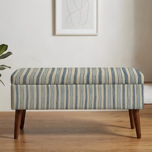 May include: A rectangular storage bench featuring a cream-colored fabric upholstery with vertical blue stripes. The bench is supported by four tapered wooden legs in a medium brown finish and includes a hinged lid for internal storage access.