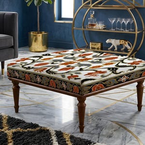 Könnte beinhalten: Ein quadratischer Hocker mit einer weißen Stoffoberfläche, die mit einem sich wiederholenden Muster aus orangefarbenen und grauen Blumenmotiven versehen ist. Der Seitenrand zeigt schwarzen Stoff mit orangefarbenen und grauen Blumenmustern.