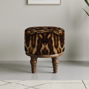 May include: A circular ottoman featuring a faux animal print in brown and tan hues. The padded top rests on a wooden base with four turned legs. This decorative furniture item is designed for interior spaces.