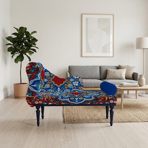 Op de afbeelding: Een chaise longue met een levendige, bedrukte stof in blauw, rood en geel. De chaise heeft donkerblauwe poten en een bijpassend blauw sierkussen. Het ontwerp heeft bloemen en geometrische motieven.