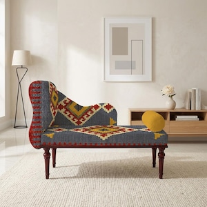 May include: A chaise lounge with a gray, red, and yellow geometric pattern. The wooden legs are dark brown. A yellow pillow rests on the seat. The chaise lounge is in a room with a white rug and a wooden cabinet.
