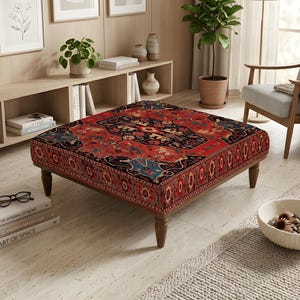 Peut inclure: Un pouf carré recouvert d'un tissu à motifs rouge, noir et bleu avec un design traditionnel à médaillon. Ce meuble est soutenu par quatre pieds en bois brun foncé et présente une surface supérieure plate et basse pour s'asseoir.