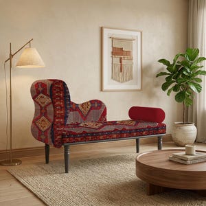 May include: A chaise lounge with a patterned red, blue, and gold fabric. The chaise has a curved back and a red bolster pillow. The legs are dark gray. A round wooden coffee table and a floor lamp are also in the room.
