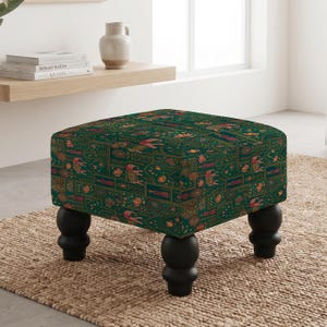 May include: A square ottoman featuring a dark green fabric upholstery with a repeating pattern of pink elephants, orange lotus flowers, and gold geometric accents. The piece is supported by four black, rounded, turned wooden legs.