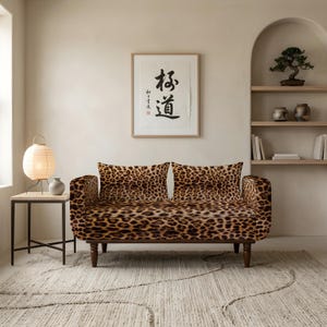May include: A two-seater sofa upholstered in a brown and black leopard print fabric. The sofa features a rectangular backrest with two matching cushions, rounded armrests, and four dark brown wooden legs. The pattern covers the entire seat.