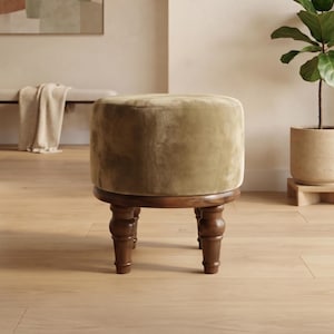 Peut inclure: Un pouf rond recouvert d'un tissu en velours vert olive. L'assise repose sur une base en bois brun foncé dotée de quatre pieds tournés de style fuseau. Le design est cylindrique avec une surface supérieure lisse et un cadre en bois robuste.