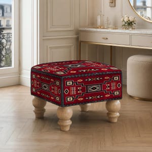 Könnte beinhalten: Ein quadratischer Hocker mit einem leuchtend roten Stoffbezug, der mit einem geometrischen Muster in Schwarz, Weiß und Hellbraun versehen ist. Das Möbelstück steht auf vier hellen, abgerundeten Holzbeinen in gedrechselter Form.