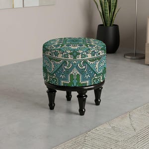 May include: A round ottoman with a patterned teal and green fabric top. The ottoman has a black wooden base and four short, black legs. The design features a repeating floral pattern. The ottoman is a decorative furniture piece.
