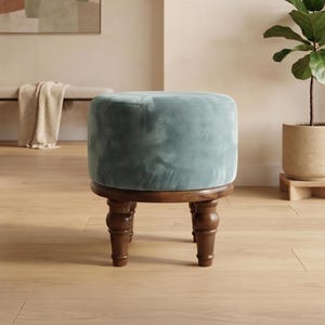 Puede incluir: Un taburete redondo con un cojín de asiento tapizado en terciopelo azul claro suave. La base está construida en madera de color marrón oscuro con cuatro patas torneadas de estilo huso que proporcionan una base firme para el asiento.