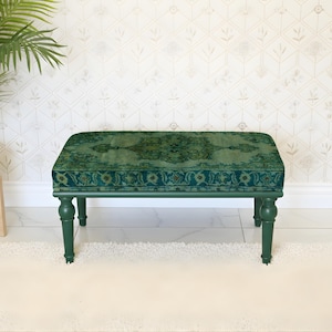 May include: A green upholstered bench with a patterned design. The bench has four turned legs and a rectangular seat. The seat cushion has a detailed, ornate pattern in shades of green and teal. The legs and frame are painted a solid, dark green.