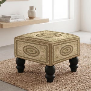 May include: A square ottoman featuring a cream-colored fabric with a dark brown ornate scrollwork pattern and central oval motifs. The piece is supported by four rounded, black wooden bun feet, providing a stable base for the upholstered seat.