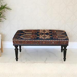 May include: A rectangular ottoman with a dark blue, patterned top and black legs. The top features a traditional rug design in shades of brown, red, and beige. The ottoman is placed on a white marble floor.